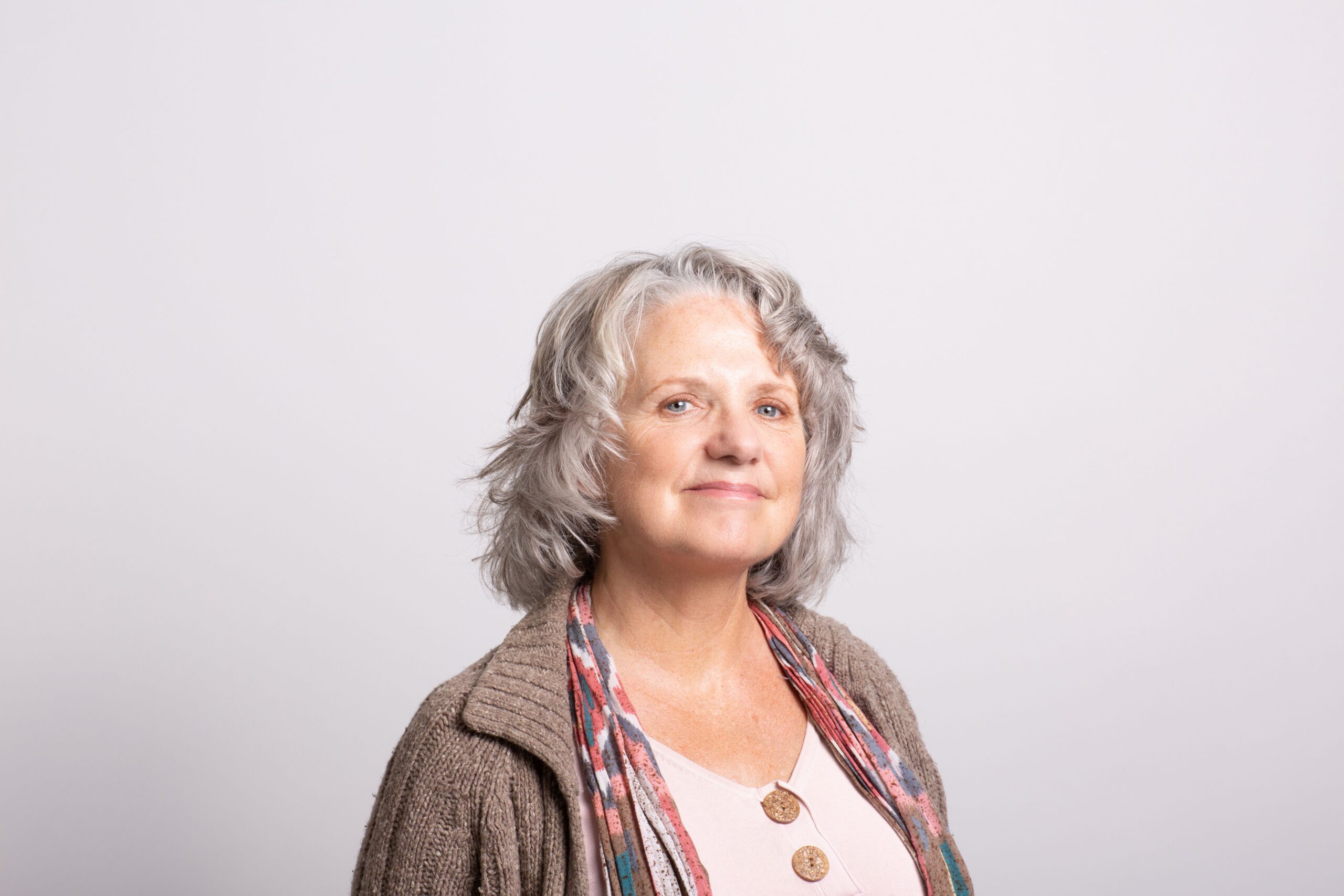 A cheerful elderly woman with gray hair smiling warmly in a neutral setting.